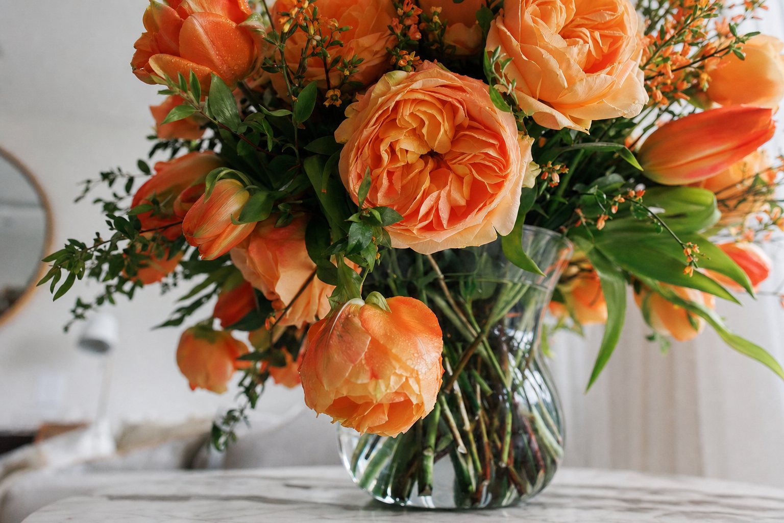 A bright orange arrangement in a glass vase on a table