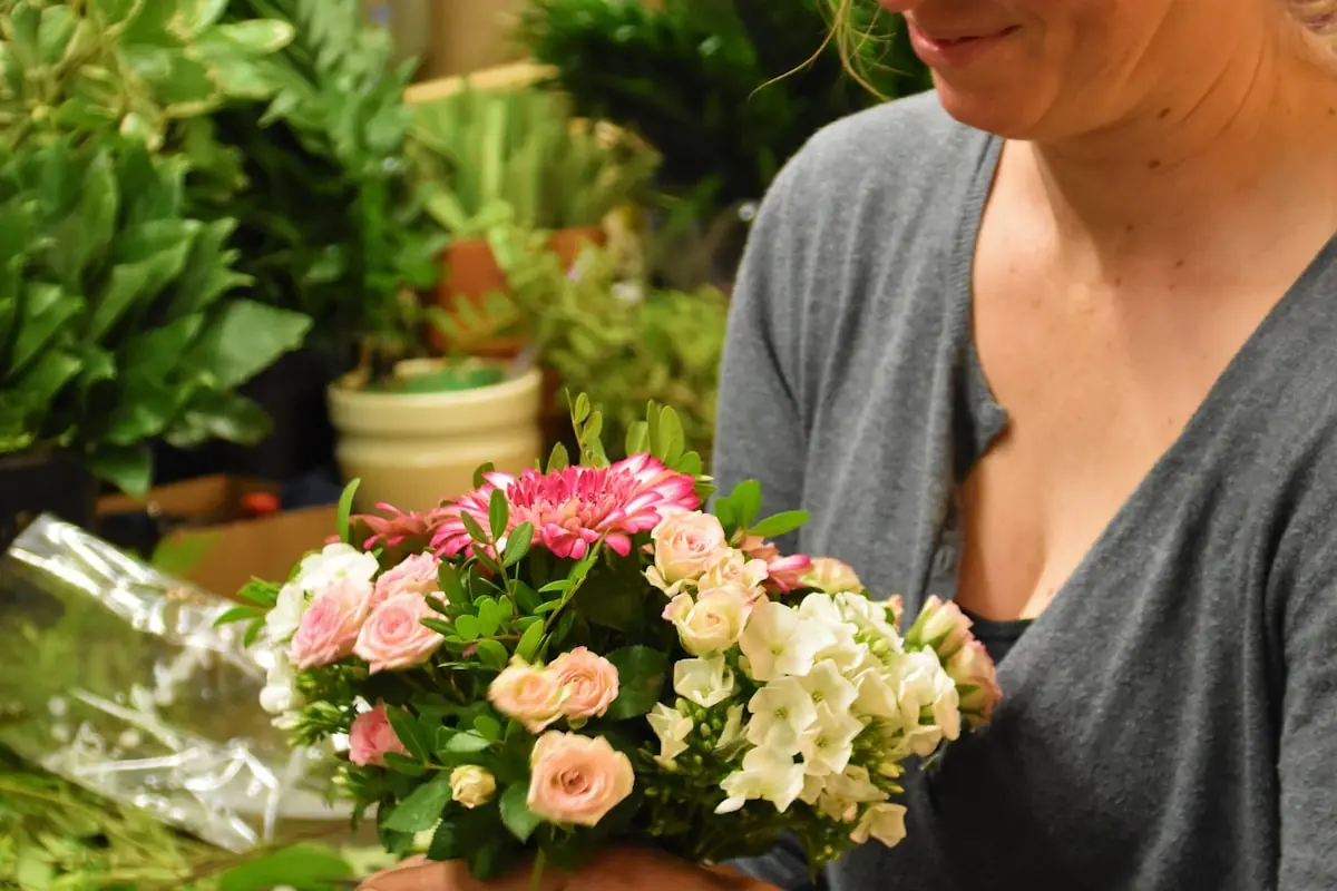 A local florist smiling over a finished bouquet of roses and phlox inside her flower shop