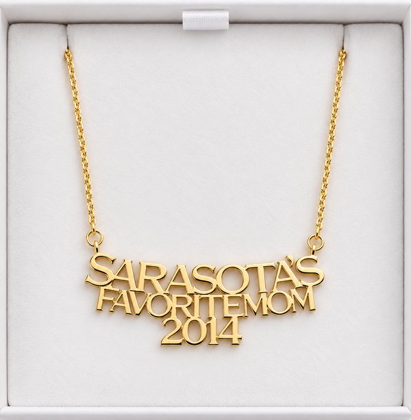 Gold pendant necklace reading Sarasota's Favorite Mom 2014 in a white presentation box